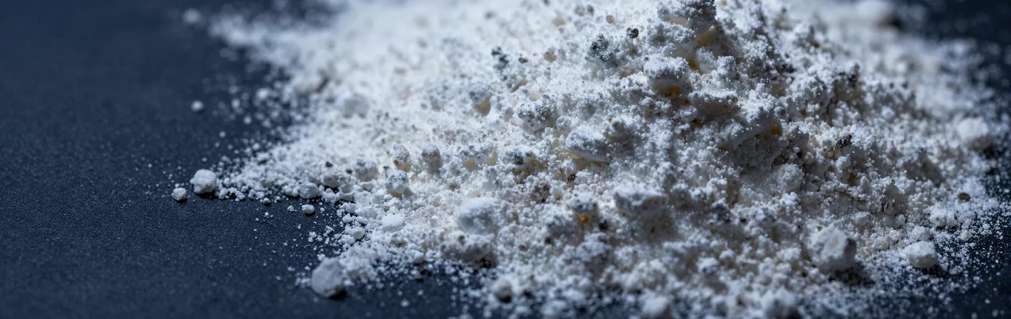 Macro de pó branco de hidroxiapatita espalhado sobre uma superfície azul-marinho, com a textura granular iluminada de lado.