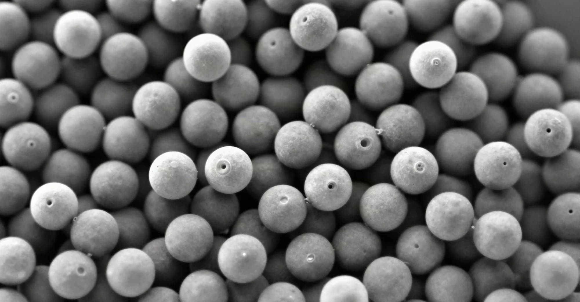 Micrografia eletrônica em tons de cinza de microesferas cerâmicas de tamanhos variados, agrupadas e bem compactadas.