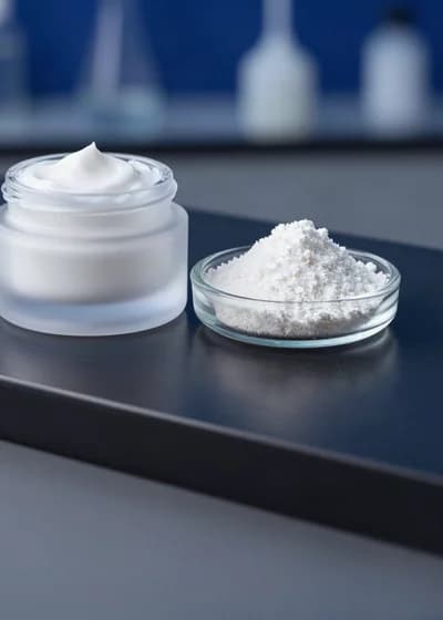 Pote de creme cosmético branco em vidro fosco, ao lado de uma placa de vidro com pó mineral fino.